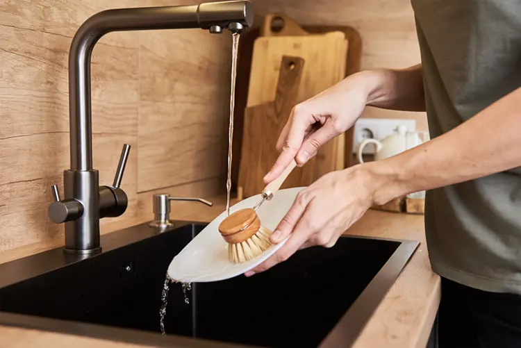 Woman washing dishes with wooden eco-friendly brush